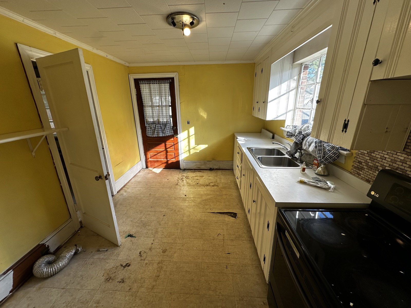 A dated kitchen with worn flooring and belongings left behind in a vacant North Carolina home