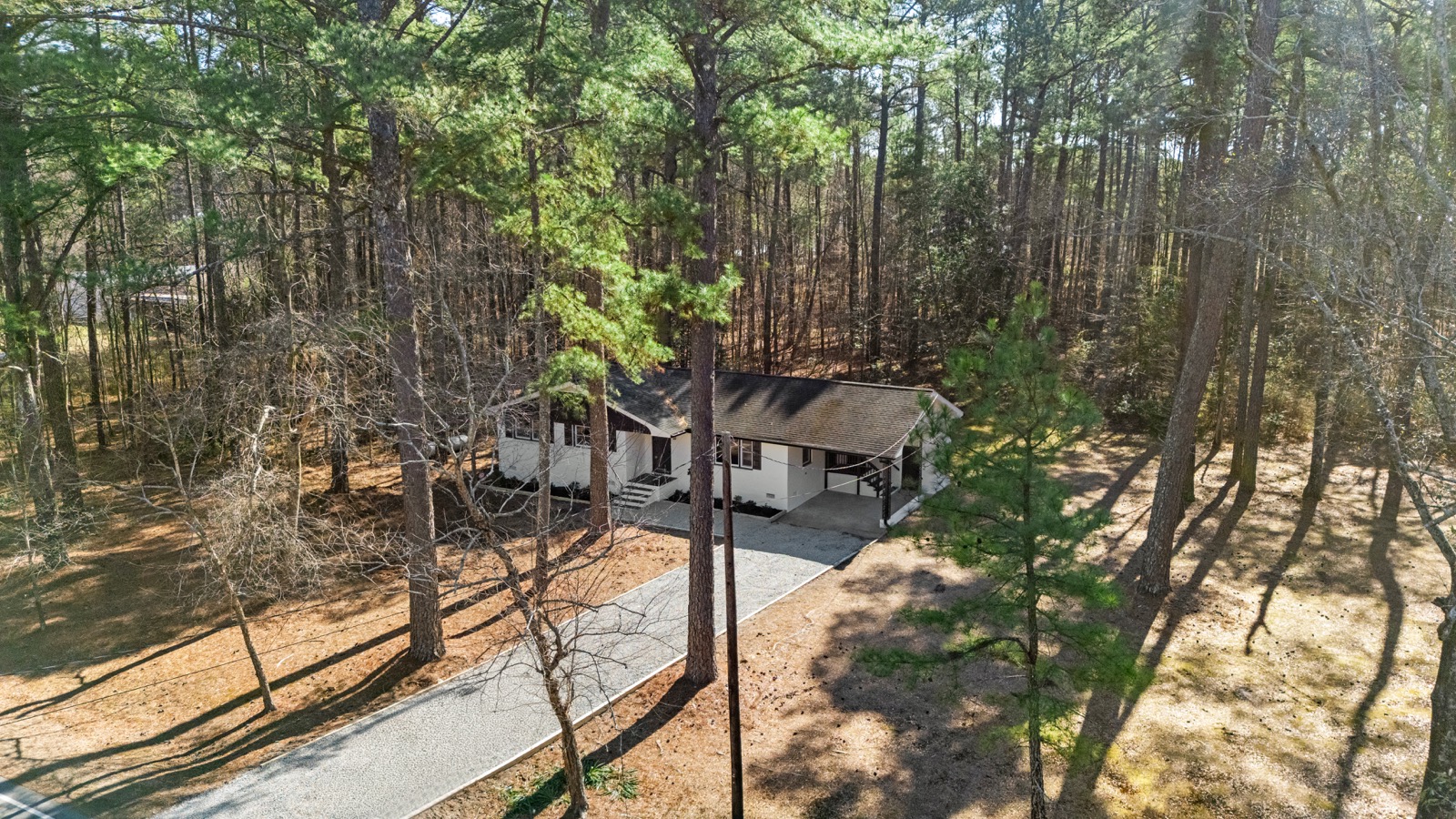 Aerial view of a North Carolina ranch surrounded by tall pine trees on a wooded lot
